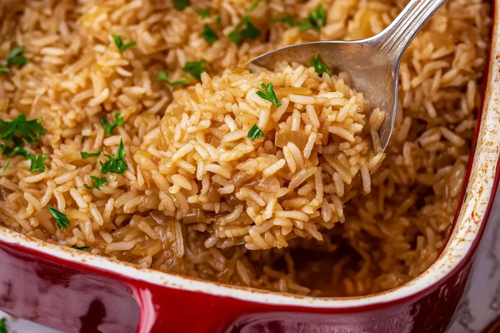 French Onion Soup Rice baked in a red ceramic dish, topped with freshly chopped parsley, served with a spoon scooping a generous portion.