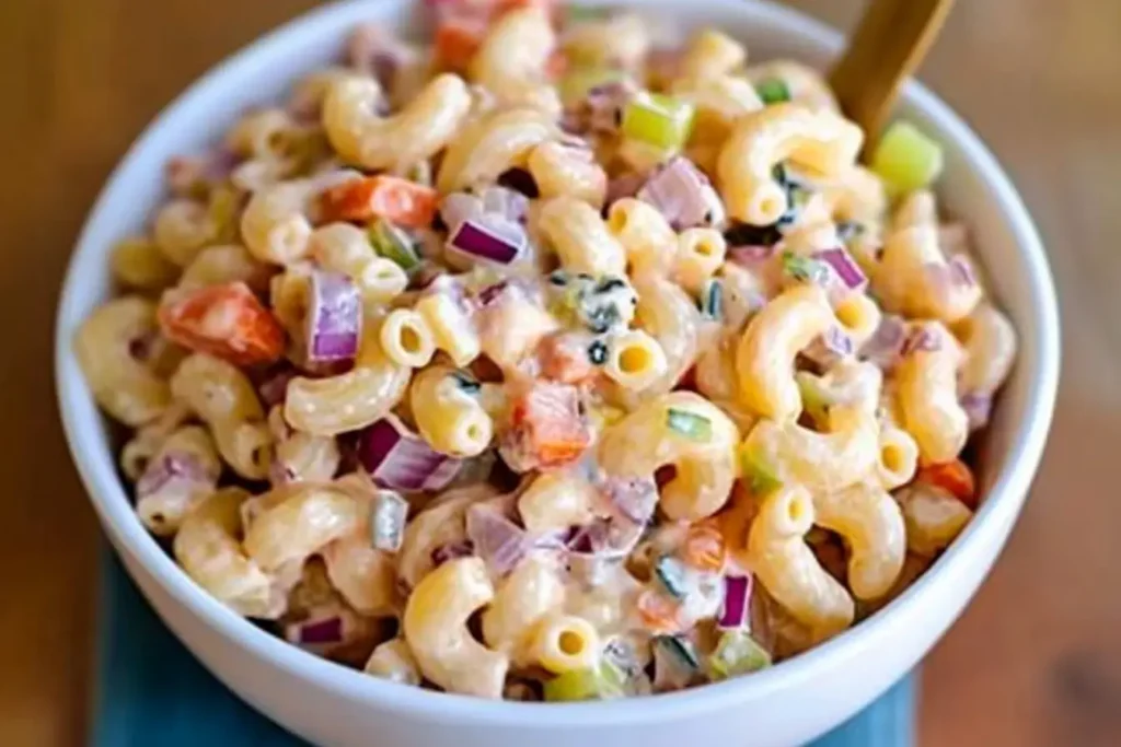 A close-up of creamy Mexican macaroni salad with elbow pasta, diced red onions, carrots, and celery, coated in a rich dressing.