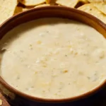 A smooth white cheese dip served in a ceramic bowl with tortilla chips, showcasing its light texture and neutral flavor.