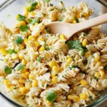 A freshly mixed Mexican Street Corn Pasta Salad in a glass bowl, with rotini pasta, corn, cilantro, and a creamy dressing ready to serve.