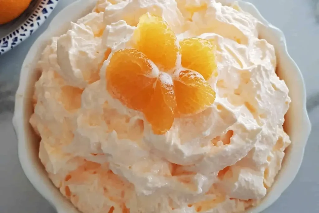 A bowl of Orange Dreamsicle Salad garnished with mandarin orange slices on top, highlighting its fluffy texture and vibrant orange color.