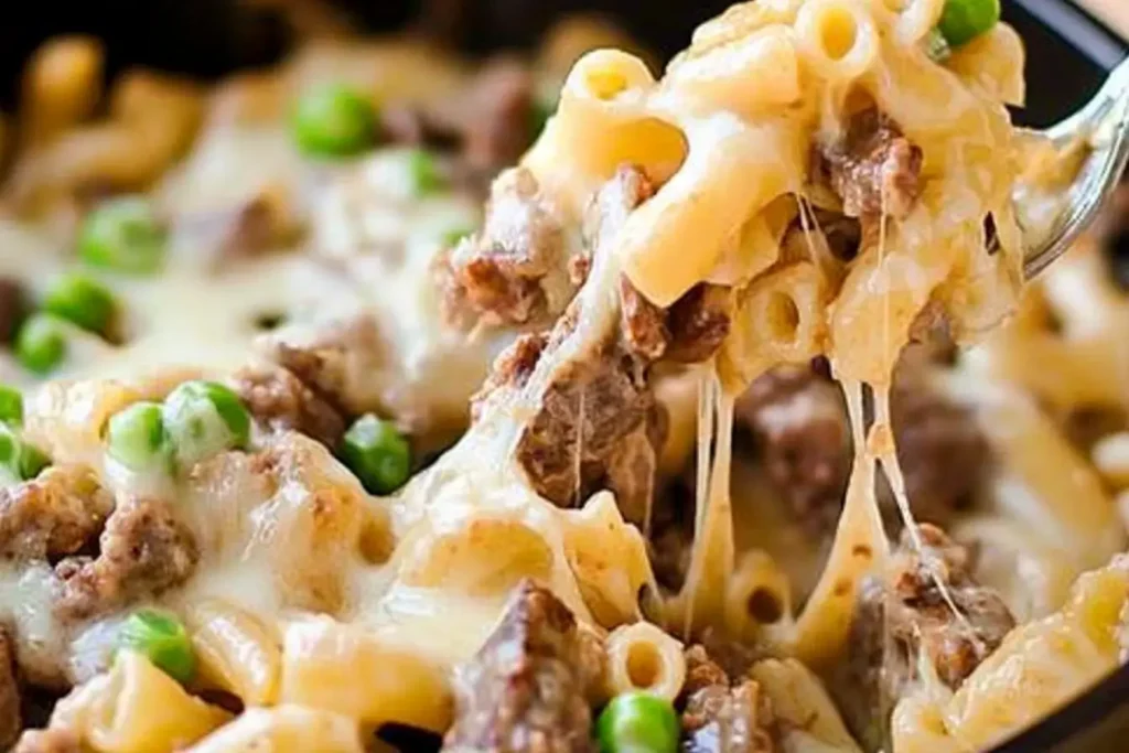 Cheesy Philly cheesesteak pasta featuring macaroni pasta, tender beef, melted cheese, and green peas being served with a fork.
