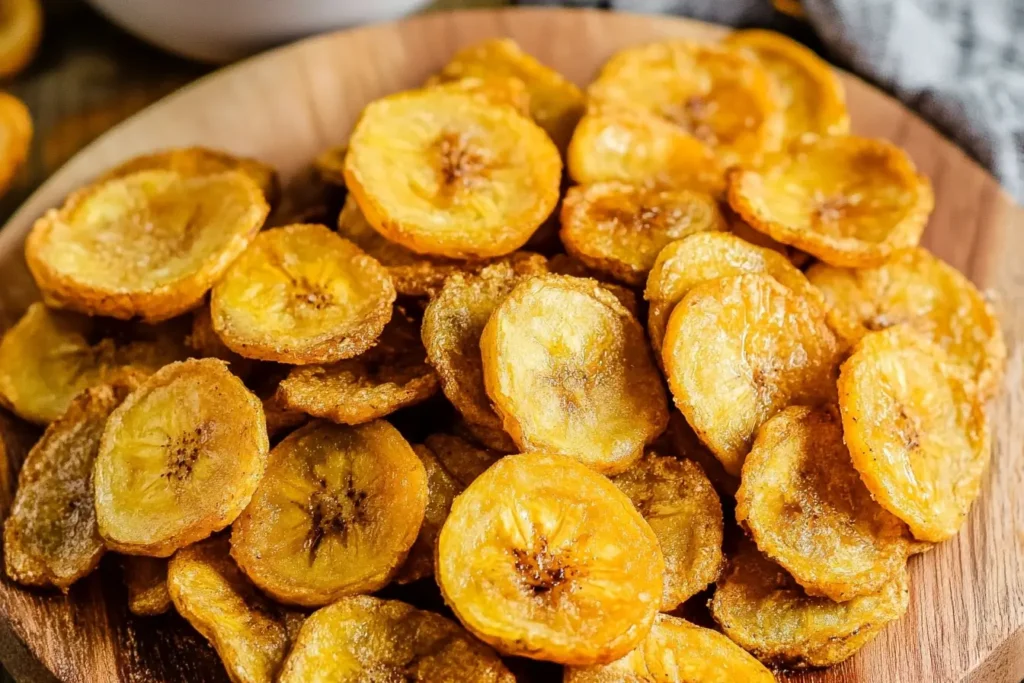 A wooden plate filled with crispy, homemade plantain chips, showcasing their even golden-brown texture and light seasoning.